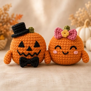 May include: Two round orange crochet pumpkins. The left pumpkin features a black top hat, a black bow tie, and a jagged black face. The right pumpkin has a pink bow with a yellow centre, a smiling face with closed eyes, and pink cheeks.