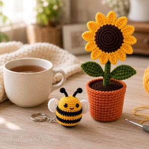 Könnte beinhalten: Eine gehäkelte Sonnenblume in einem braunen Topf und ein gehäkelter Bienen-Schlüsselanhänger mit schwarzen und gelben Streifen, weißen Flügeln und schwarzen Fühlern. Die Sonnenblume hat eine dunkelbraune Mitte und leuchtend gelbe Blütenblätter. Der Text HookedBloomPattern ist sichtbar.