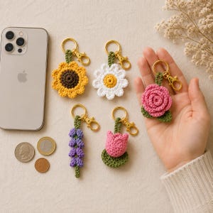 May include: A collection of five handmade crochet flower keychains featuring a yellow sunflower, a white daisy, a pink rose, a purple lavender sprig, and a pink tulip, each attached to a gold-toned metal lobster clasp and keyring.