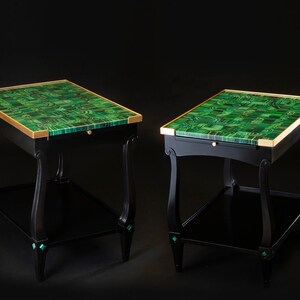 May include: Two black end tables with green malachite tops and gold trim. The tables have a lower shelf and decorative accents on the legs.