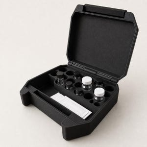 May include: A black, rectangular, hinged storage case with a foam interior featuring multiple circular cutouts. The case contains several small, clear glass vials with black or white screw-on caps and one rectangular white packet in a slot.