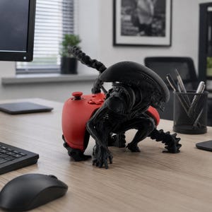 Può includere: Una figura nera di Xenomorfo della serie Alien progettata come supporto per controller, in posizione accovacciata con una lunga coda, che tiene un controller per videogiochi rosso brillante tra le braccia e le gambe su una scrivania.