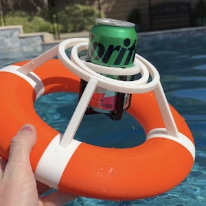Könnte beinhalten: Ein leuchtend orange-weißer, kreisförmiger Rettungsring mit einer zentralen weißen Kunststoff-Getränkehalterung. Eine grüne und silberne Sprite-Dose steckt sicher in der Halterung, die zum Schwimmen auf der Wasseroberfläche konzipiert ist.