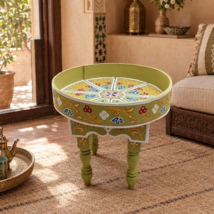 Peut inclure: Une table d'appoint ronde en bois vert olive avec un bord surélevé et trois pieds tournés. Le plateau et les côtés extérieurs sont peints à la main avec des motifs floraux et géométriques complexes dans des tons de jaune, rouge, blanc et bleu.