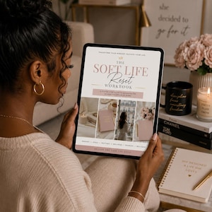 May include: A digital tablet displaying a workbook cover titled The Soft Life Reset Workbook. The cover features a crown icon, text about transforming your mindset, and three photo panels showing a candle, a notebook, and a person by a window.