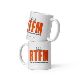 Puede incluir: Dos tazas de cerámica blanca apiladas verticalmente. Cada taza presenta un icono de libro abierto azul sobre el texto grande en naranja RTFM. Debajo, el texto dice Google isn't tattooed on my forehead. TECH SUPPORT ANONYMOUS.