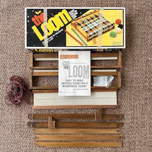 May include: A 20-inch table top weaving loom kit by NSI, including a cardboard box with product imagery, a wooden loom frame with metal teeth, a set of wooden shuttles, a bundle of red yarn, and an instruction manual titled The Loom.
