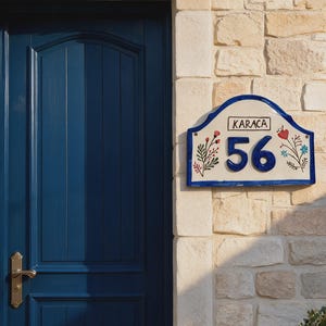 Pode incluir: Uma placa de cerâmica retangular para número de casa com borda azul, apresentando o número 56 em grandes dígitos azuis e o texto KARACA em uma caixa preta. A placa é decorada com motivos florais pintados à mão nas cores vermelho, azul e verde.