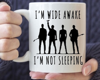 May include: White ceramic coffee mug with a black silhouette of four people and the text "I'm wide awake I'm not sleeping".