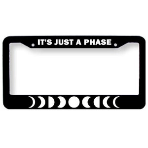 May include: Black license plate frame with white text that reads "It's Just A Phase." The frame has a row of eight white crescent moons along the bottom.