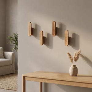 Puede incluir: Cuatro ganchos de pared de madera de color marrón claro con forma rectangular redondeada y vertical. Los ganchos están montados en una disposición escalonada sobre una pared lisa, con un acabado de madera natural y lisa.