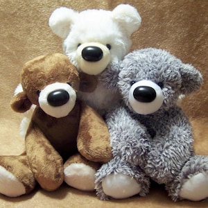 May include: Three plush teddy bears sitting together. One bear is white with smooth fur, one is brown with short plush fur, and one is grey with textured, shaggy fur. Each bear features a white muzzle, a round black nose, and white paw pads.