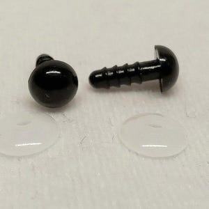 May include: Two black plastic safety eyes with smooth, rounded heads and ribbed stems for secure attachment, accompanied by two clear, circular plastic washers designed to lock the eyes in place for plush toys or craft projects.