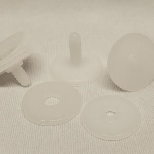 May include: A set of white plastic snap fasteners consisting of several components. The pieces include rounded caps with protruding stems and flat circular washers with a central hole, designed for joining fabric layers together securely.
