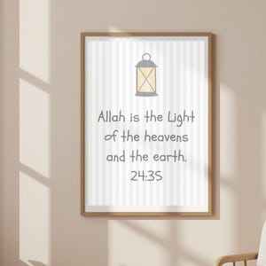 May include: A framed vertical wall art print featuring a light yellow lantern icon at the top, centered above the text "Allah is the Light of the heavens and the earth. 24:35" in dark gray, set against a background of vertical white and light gray stripes.