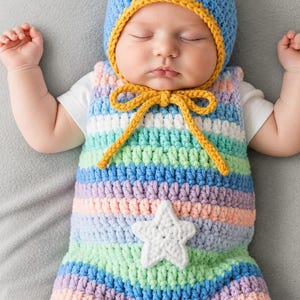Pode incluir: Um conjunto de bebé em croché composto por um macacão sem mangas às riscas e um gorro a condizer. O macacão tem riscas horizontais em azul pastel, verde, roxo e pêssego, com uma aplicação de estrela branca em croché. O gorro azul tem um rebordo amarelo.