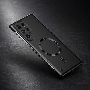 Può includere: Una custodia per smartphone nero opaco dotata di un sistema di allineamento magnetico circolare sul retro, un ritaglio per una fotocamera a più lenti e un piccolo emblema circolare vicino al bordo inferiore, per un dispositivo mobile elegante.