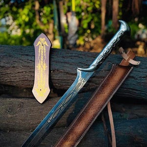 Puede incluir: Una espada de metal plateado con un mango curvo ornamentado y grabados intrincados en la hoja. Junto a la espada hay una funda de cuero marrón con una correa clara y una placa marrón oscuro separada con patrones decorativos de color dorado.