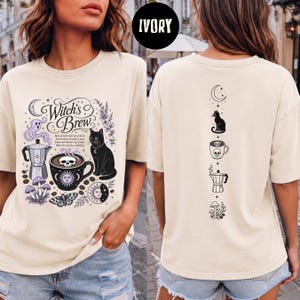 May include: An ivory t-shirt featuring a front graphic with a coffee pot, a cup with a skull, a black cat, mushrooms, and the text Witch's Brew. The back graphic displays a vertical column of icons including a crescent moon, cat, skull mug, coffee pot, and mushrooms.