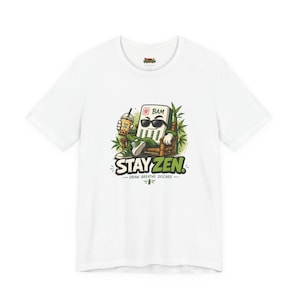 Könnte beinhalten: Ein weißes Kurzarm-T-Shirt mit einer Grafik einer Mahjong-Stein-Figur mit Sonnenbrille, die in einem Bambusstuhl sitzt und ein Boba-Getränk hält. Der Text lautet STAY ZEN sowie DRAW. BREATHE. DISCARD. und zeigt grüne Bambusblätter im Hintergrund.