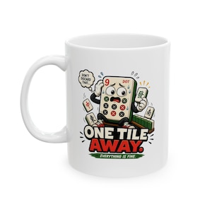 May include: A white ceramic mug featuring a cartoon illustration of a stressed 9-dot mahjong tile with arms and legs. The graphic includes the text "DON'T DISCARD THAT...", "ONE TILE AWAY.", and "EVERYTHING IS FINE." surrounded by other mahjong tiles.