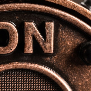 May include: Close-up of a copper-colored metal switch with the word "ON" embossed on it. The switch has a black knob and a textured surface.