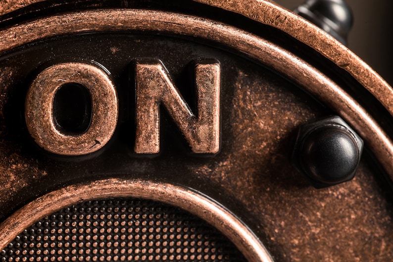 May include: Close-up of a copper-colored metal switch with the word "ON" embossed on it. The switch has a black knob and a textured surface.