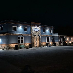 May include: A blue building with a sign that reads "The Rustic Tavern" at night. The building has a stone facade and is lit by several lights.