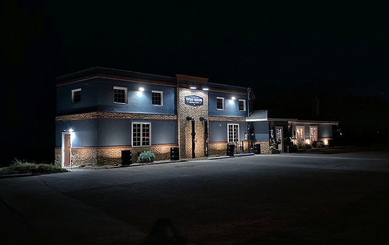 May include: A blue building with a sign that reads "The Rustic Tavern" at night. The building has a stone facade and is lit by several lights.