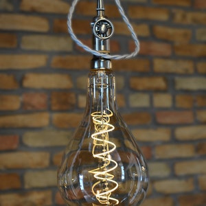 May include: A clear glass light bulb with a coiled filament hangs from a silver cord and a metal fixture. The bulb is illuminated and the filament glows brightly.