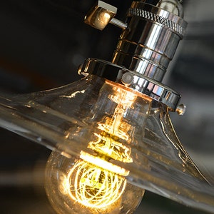 May include: A clear glass lampshade with a chrome socket and a light bulb with a coiled filament. The light bulb is turned on and glowing.