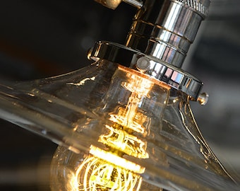 May include: A clear glass lampshade with a chrome socket and a light bulb with a coiled filament. The light bulb is turned on and glowing.