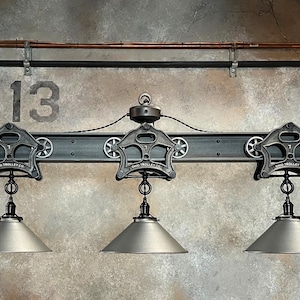 May include: Three industrial-style pendant lights with black metal shades hanging from a black metal beam with three black metal pulleys. The beam is attached to the ceiling with chains. The pulleys have the text "Ohio Trolley Co." on them. The numbers "13" and "8" are painted on the wall behind the lights.