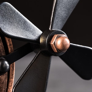 Pode incluir: Close-up de um ventilador de metal preto com uma porca de cor cobre e uma tampa de cor cobre na extremidade da p&aacute; do ventilador.