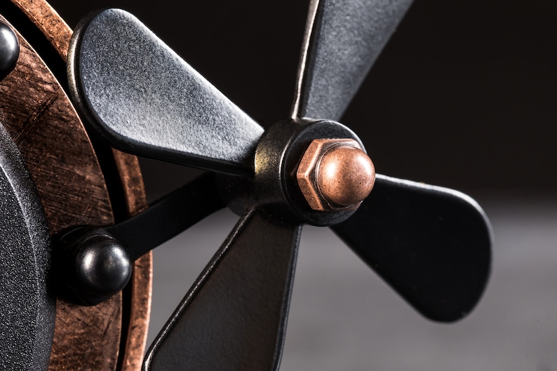 Pode incluir: Close-up de um ventilador de metal preto com uma porca de cor cobre e uma tampa de cor cobre na extremidade da p&aacute; do ventilador.