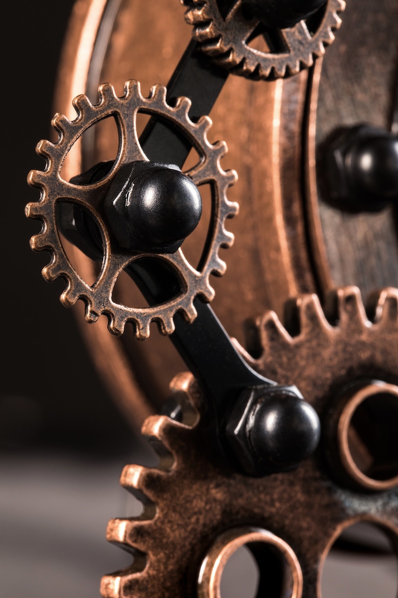 Pode incluir: Close-up de um conjunto de engrenagens de bronze interligadas com detalhes pretos. As engrenagens s&atilde;o conectadas por uma haste de metal preta.