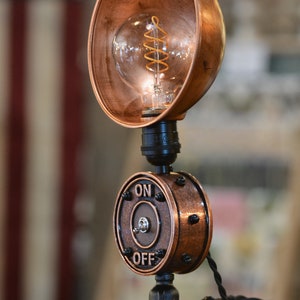 May include: A copper steampunk style table lamp with a round copper shade and a black switch with the words "ON" and "OFF" on it.