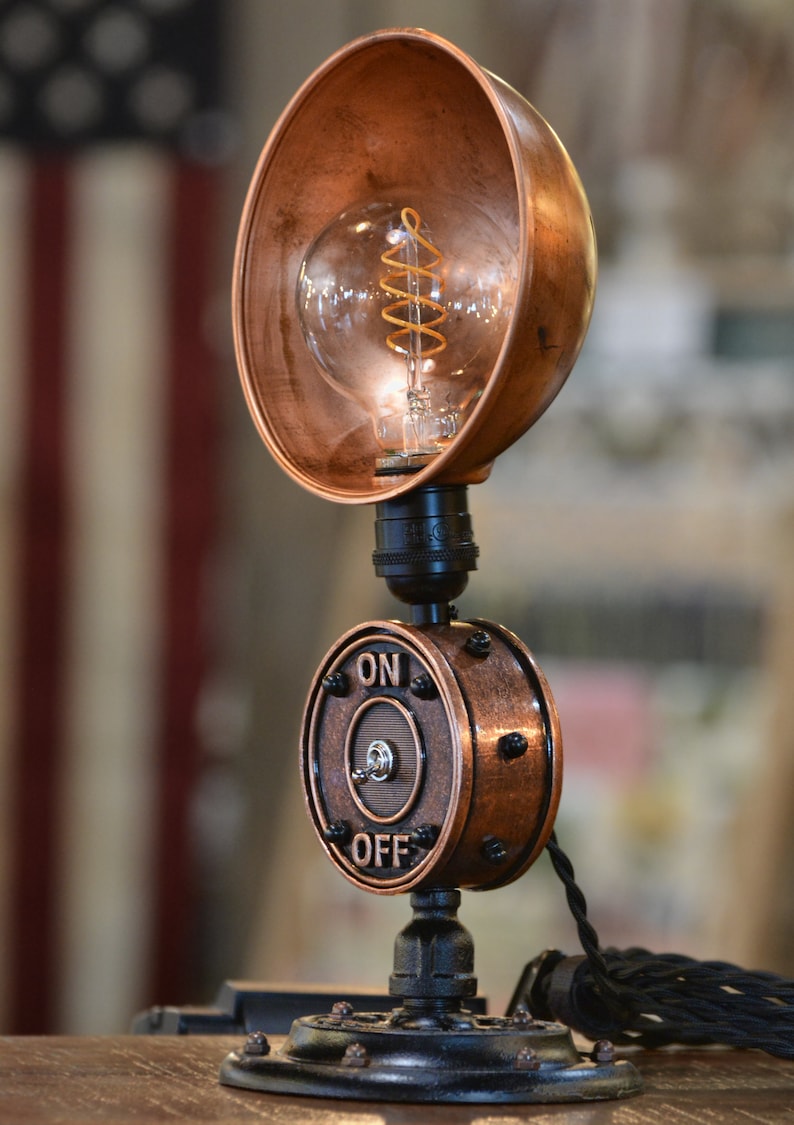 May include: A copper steampunk style table lamp with a round copper shade and a black switch with the words "ON" and "OFF" on it.
