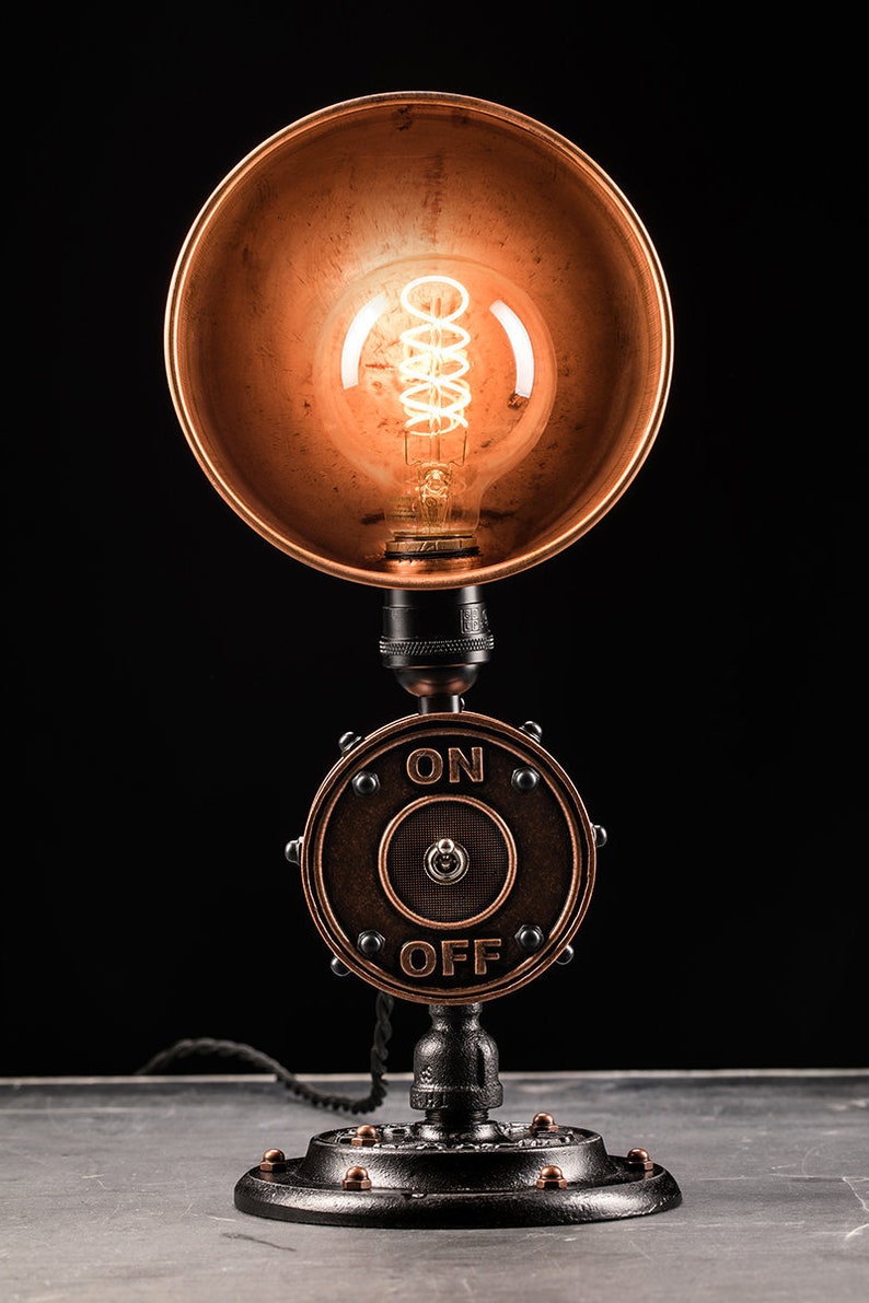 May include: A steampunk-style table lamp with a copper shade and a black metal base. The base features a round switch with the words "ON" and "OFF" printed on it.