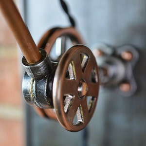 K&ouml;nnte beinhalten: Nahaufnahme einer industriellen Lampe aus Kupfer und schwarzem Metall mit einem Zahnrad-Einstellrad.