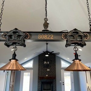 May include: A rustic industrial style ceiling light fixture with two copper-toned shades hanging from a black metal beam with the number 80822 printed on it.