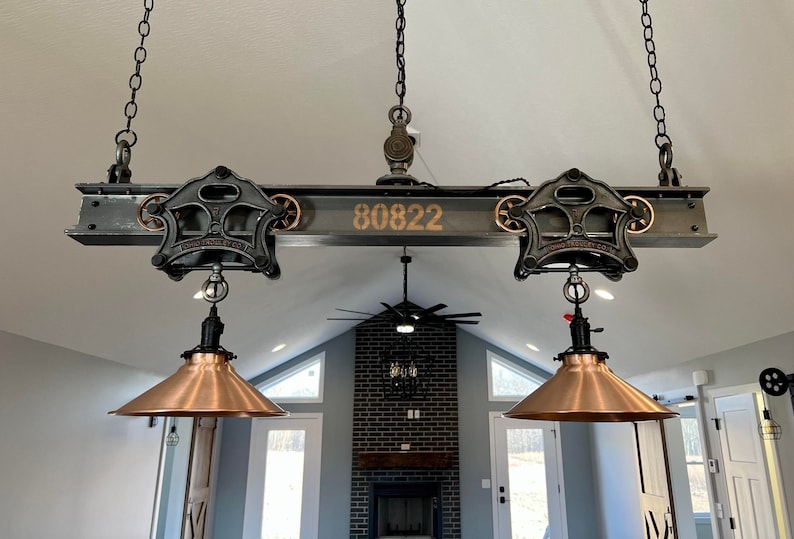 May include: A rustic industrial style ceiling light fixture with two copper-toned shades hanging from a black metal beam with the number 80822 printed on it.