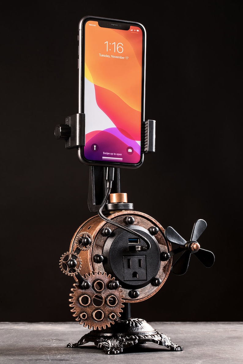 Pode incluir: Uma esta&ccedil;&atilde;o de carregamento de telefone estilo steampunk com acabamento preto e cobre. Possui uma tomada de energia integrada, uma porta USB e um suporte para telefone. A esta&ccedil;&atilde;o &eacute; montada em uma base de metal preto com engrenagens decorativas.