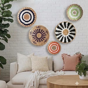 May include: Five round woven wall baskets featuring various patterns and colours, including a blue and white spiral, a green and white swirl, a black and white zigzag design, a purple sunburst pattern, and a small orange and white concentric circle.