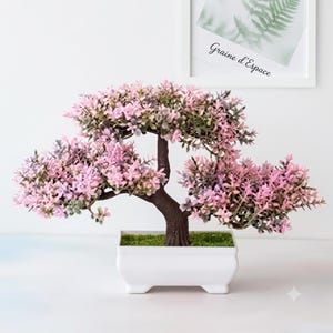 Peut inclure: Un bonsaï artificiel avec un tronc et des branches brun foncé recouverts de petites feuilles rose clair et vertes. L'arbre est planté dans un pot en céramique blanc rectangulaire rempli de fausse mousse verte, formant une plante décorative.