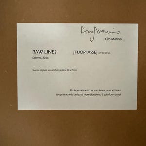 Op de afbeelding: Een witte rechthoekige informatiekaart met zwarte tekst, voorzien van de handtekening van Ciro Marino, de titel RAW LINES [FUORI ASSE], de datum 2026, de tekst Stampa digitale su carta fotografica, 50 x 70 cm en een korte Italiaanse zin.