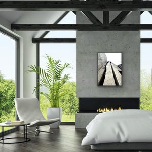 Op de afbeelding: Een rechthoekige wandkunstprint met een zwart-wit architectuurfoto vanuit een laag standpunt van gestructureerde betonconstructies met diepe verticale groeven, ingelijst in een dunne zwarte lijst aan een grijze betonnen muur.