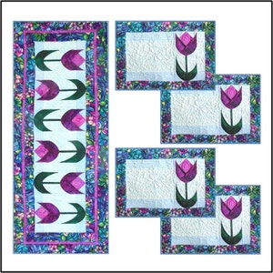 Peut inclure: Un ensemble de cinq chemins de table matelassés avec un motif floral composé de tulipes roses et violettes sur fond blanc. Les chemins de table ont une bordure bleue et verte avec un motif floral.