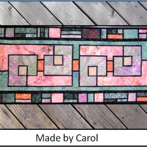 Puede incluir: Una colcha colorida con un dise&ntilde;o geom&eacute;trico que presenta cuadrados y rect&aacute;ngulos en tonos de rosa, verde y marr&oacute;n. La colcha est&aacute; enmarcada por un borde negro y tiene el texto "Made by Carol" en la parte inferior.
