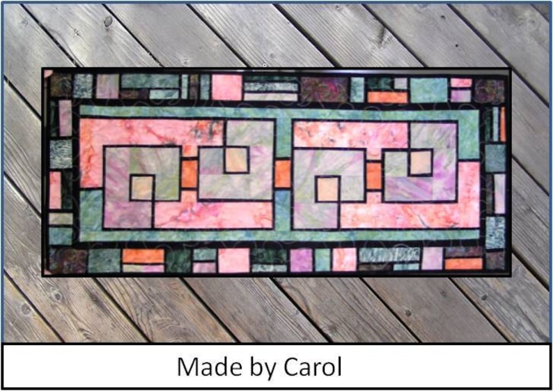 Puede incluir: Una colcha colorida con un dise&ntilde;o geom&eacute;trico que presenta cuadrados y rect&aacute;ngulos en tonos de rosa, verde y marr&oacute;n. La colcha est&aacute; enmarcada por un borde negro y tiene el texto "Made by Carol" en la parte inferior.